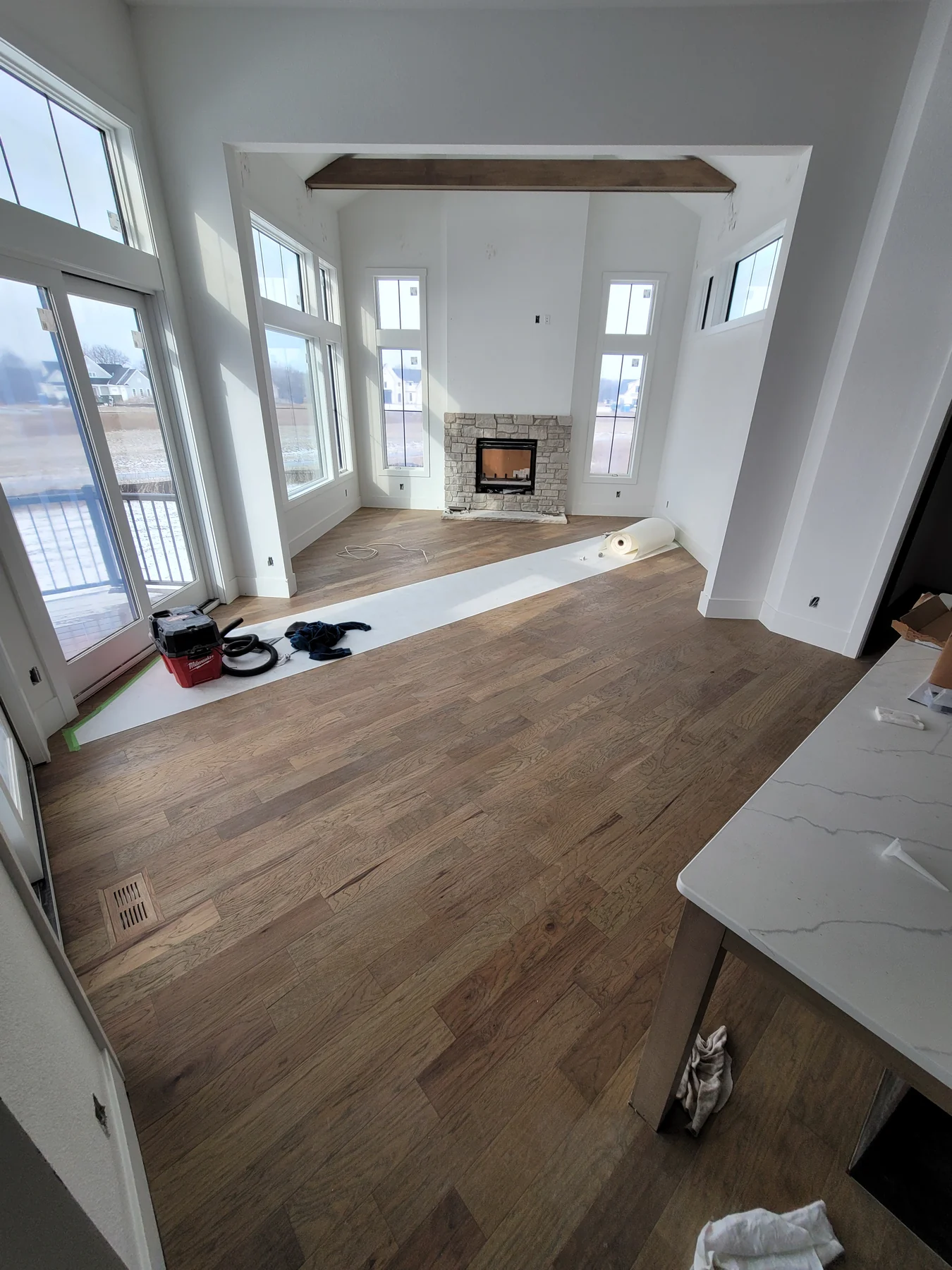 Engineered hardwood flooring through a tall living room with a fireplace and large windows