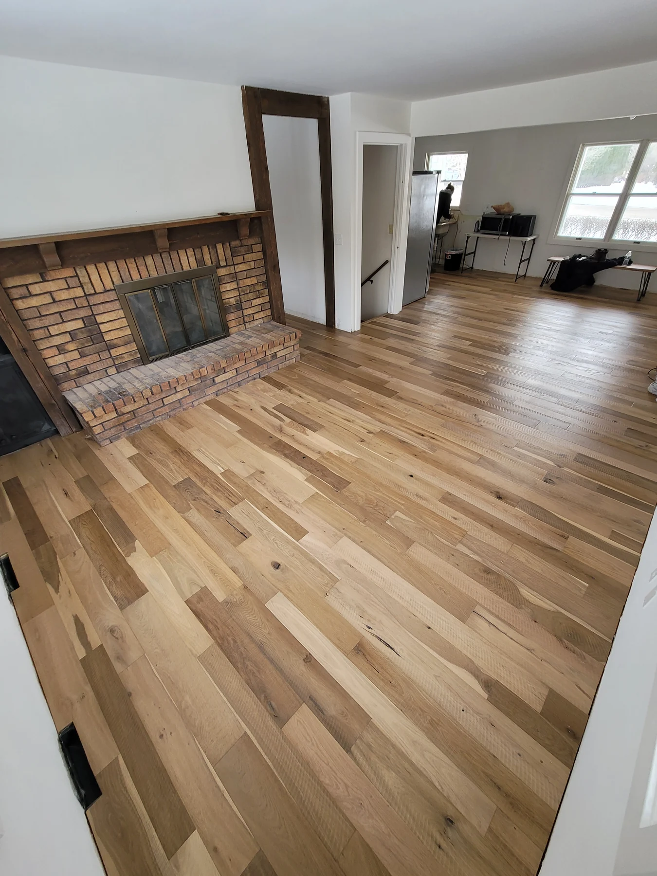 Mixed-width engineered hardwood flooring beside a brick fireplace and into an adjoining room