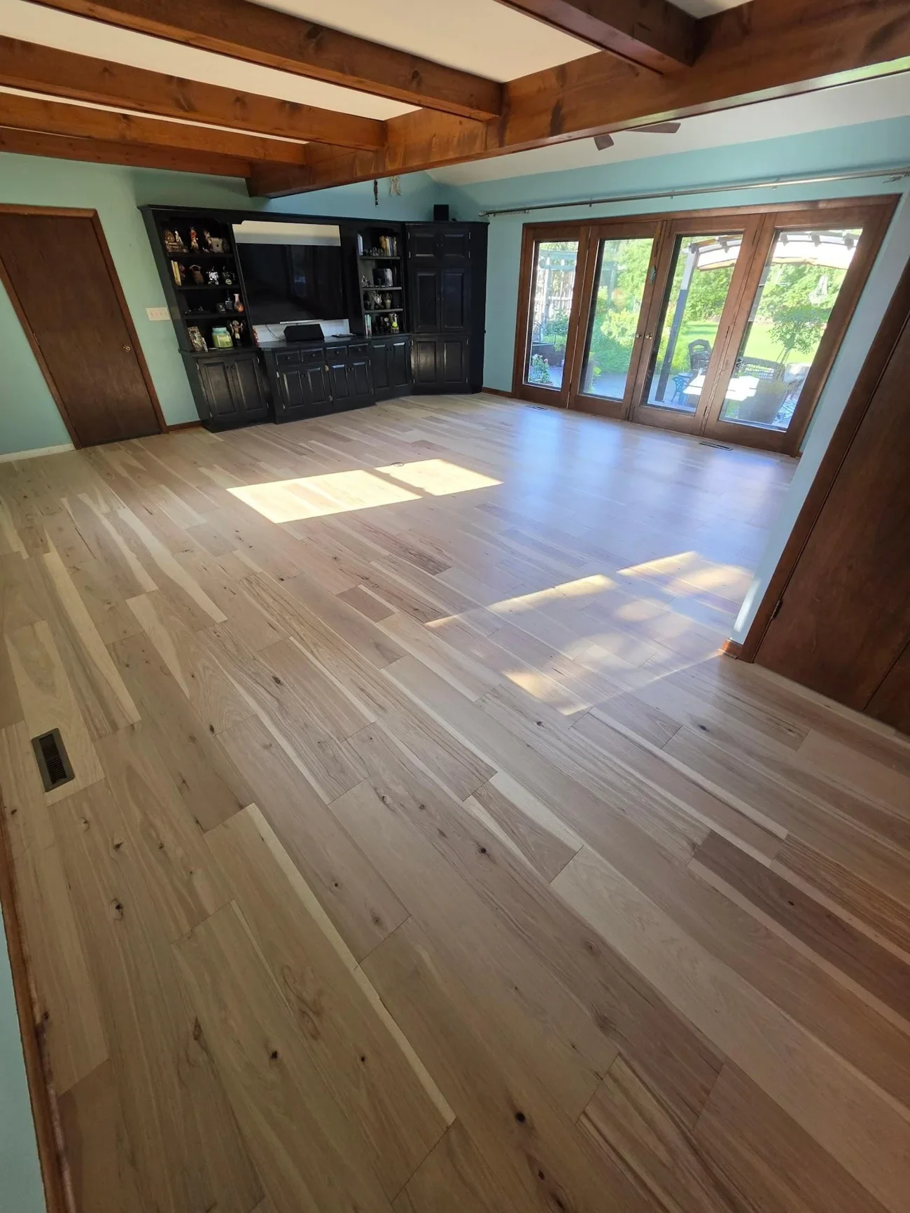 Exposed wood beams and a stone fireplace above a light wood-look plank floor