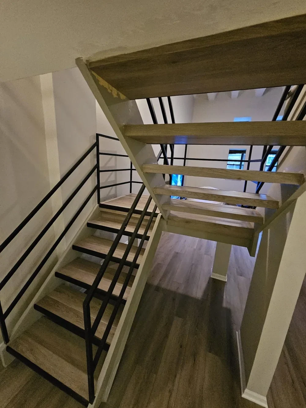 View down a staircase with wood-look treads and dark railing