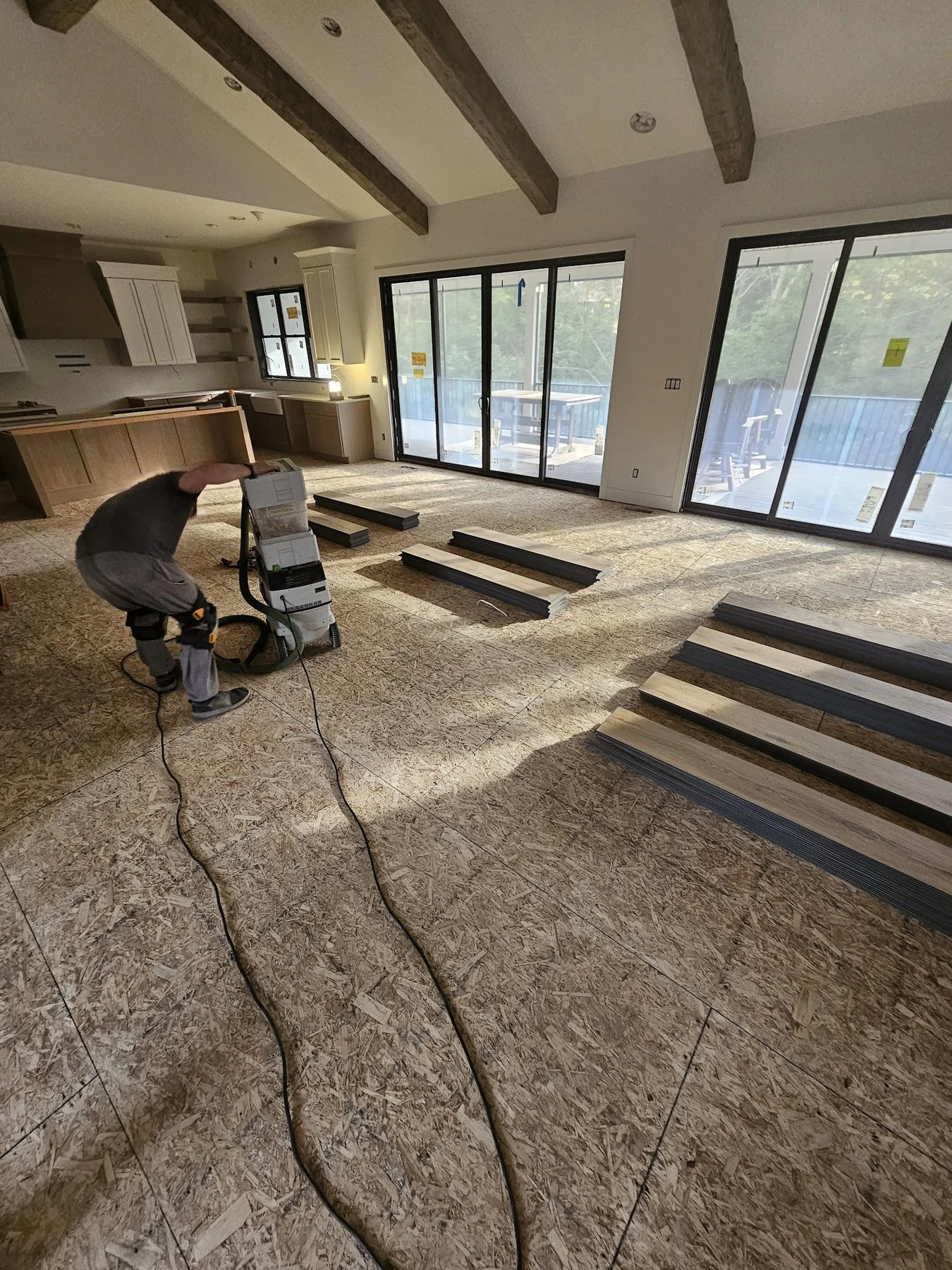 A crew member with flooring equipment and boards staged on an exposed wood subfloor