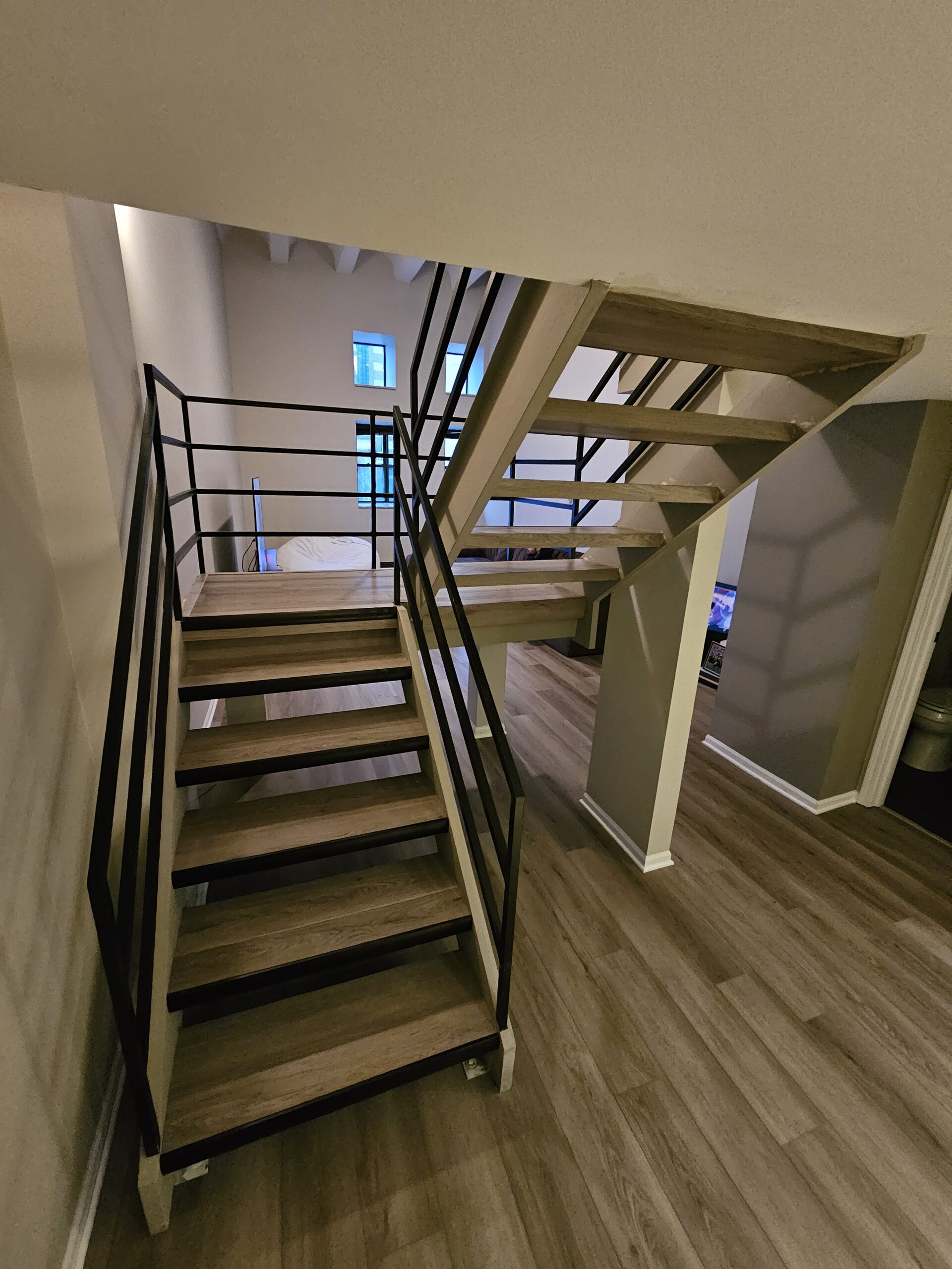 Open wood-look staircase with black metal rails and coordinated plank flooring below